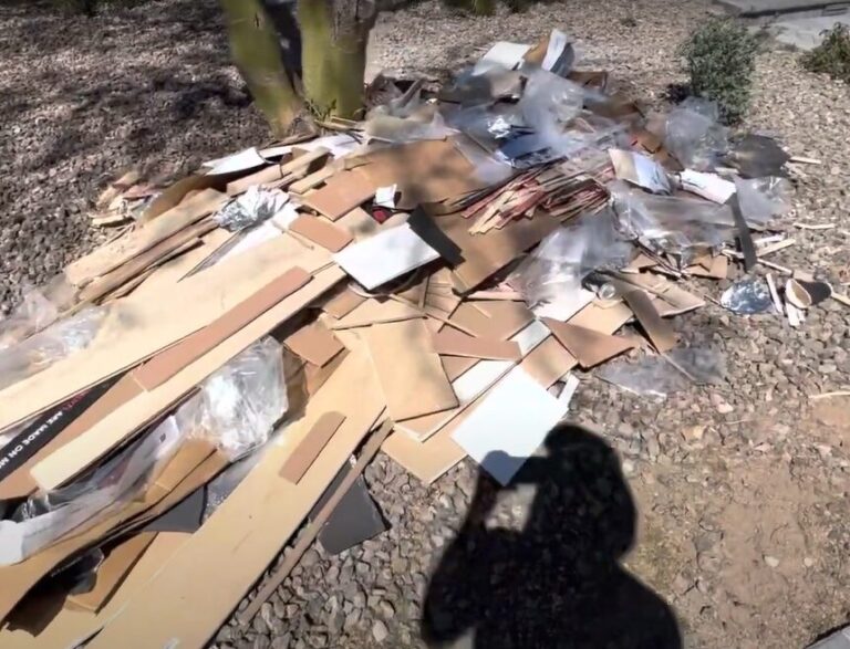 Construction Junk Removal : A large pile of cardboard boxes, plastic bags, and other discarded materials scattered on a gravel surface in a yard.