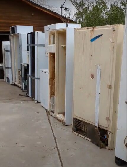 Appliance Removal In Wichita KS: A row of discarded refrigerators lined up in a driveway. Some refrigerators are missing doors or have broken parts, while others are seemingly intact.