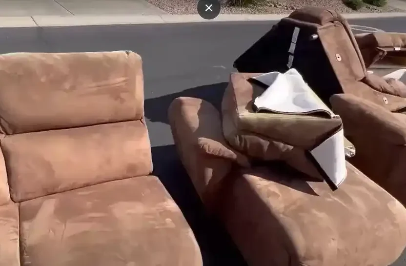 Furniture removal in wichita KS : Several discarded recliners and sofas are lined up on a residential street. The furniture is covered in dust and appears to be damaged or worn out.