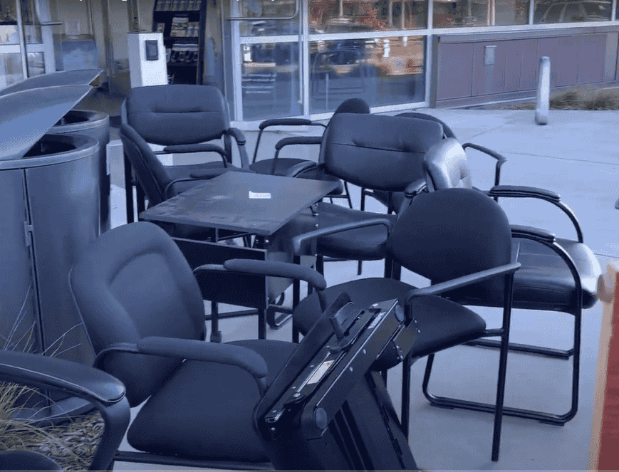 Office Cleanout in Wichita KS : A group of discarded office chairs and a small table sitting outside a building. The chairs are mostly black with fabric seats, and some have wheels.